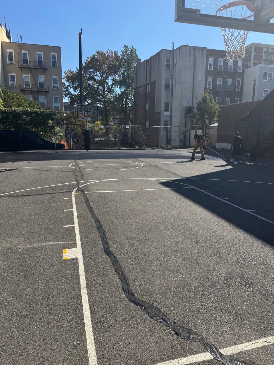 Basketball court asphalt surface after crack filling is complete with sealcoating in progress by Sterling Pavement crew in New Jersey